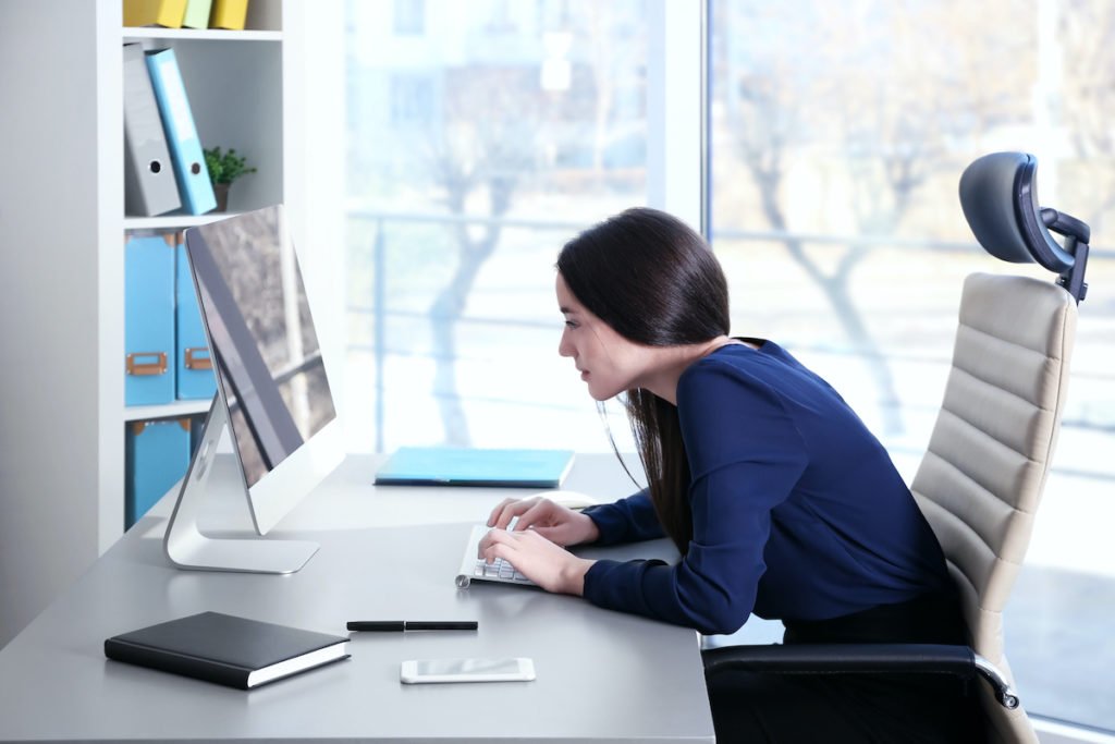 lady with poor posture leaning over office desk to type on her computer keyboard